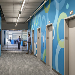 men walk through the third floor elevator lobby with a blue feature wall with green and white accents