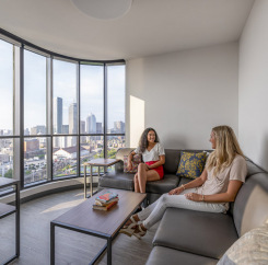 Two women hanging out in the common area with a view of the Boston skyline out the window